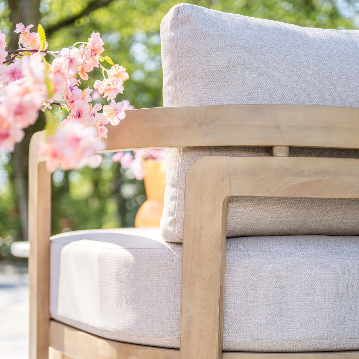 Een lichte fauteuil met kussens en roze bloemen ervoor.