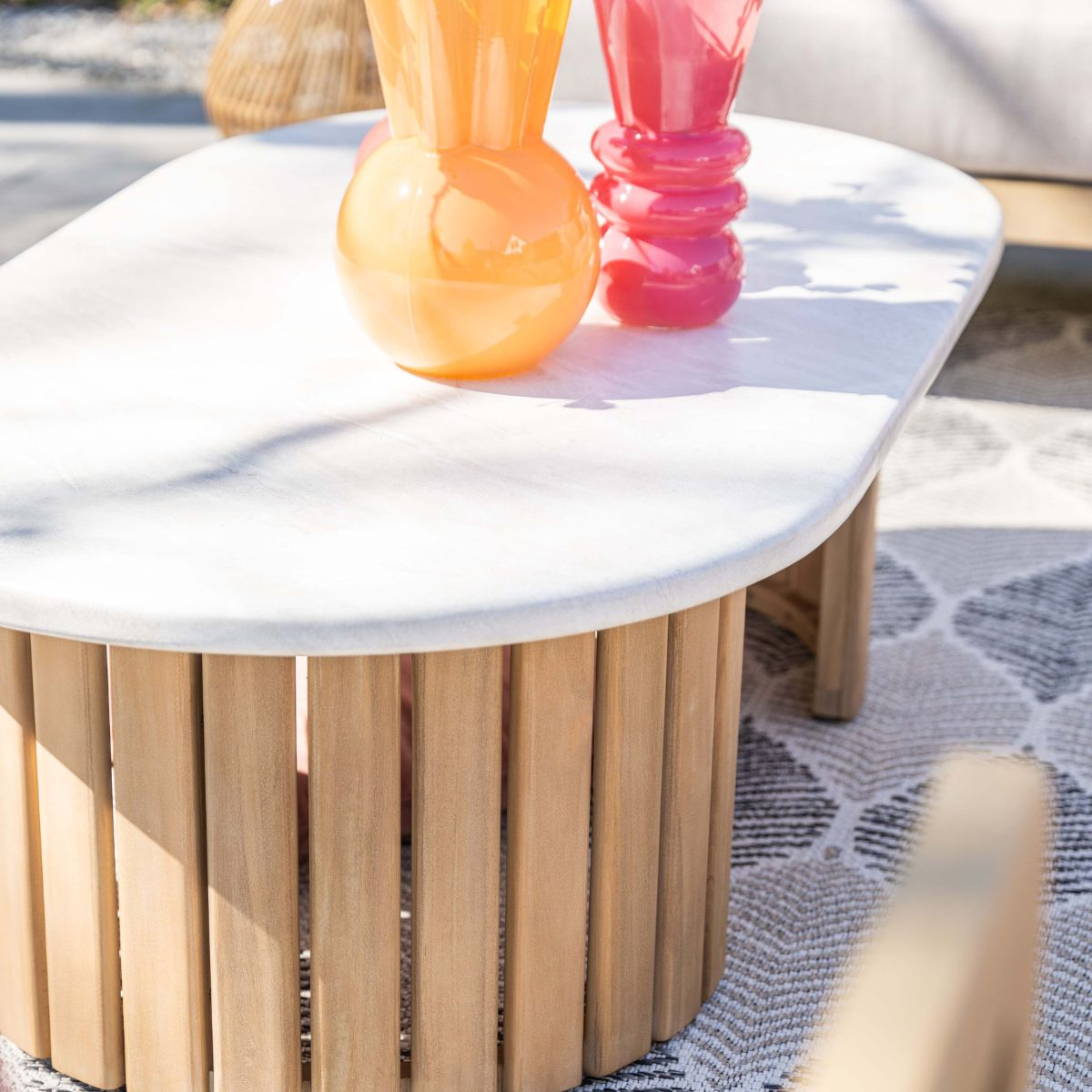 A white oval table with a wooden base and two colorful glass vases.