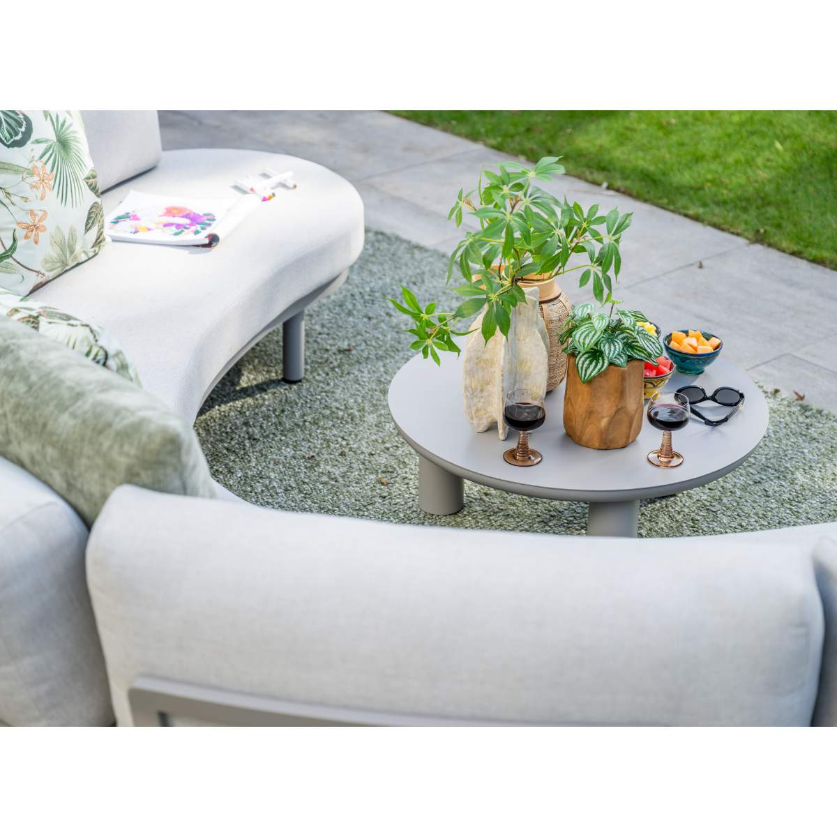 Gray outdoor table with glasses, plants, fruit bowls, and sunglasses.