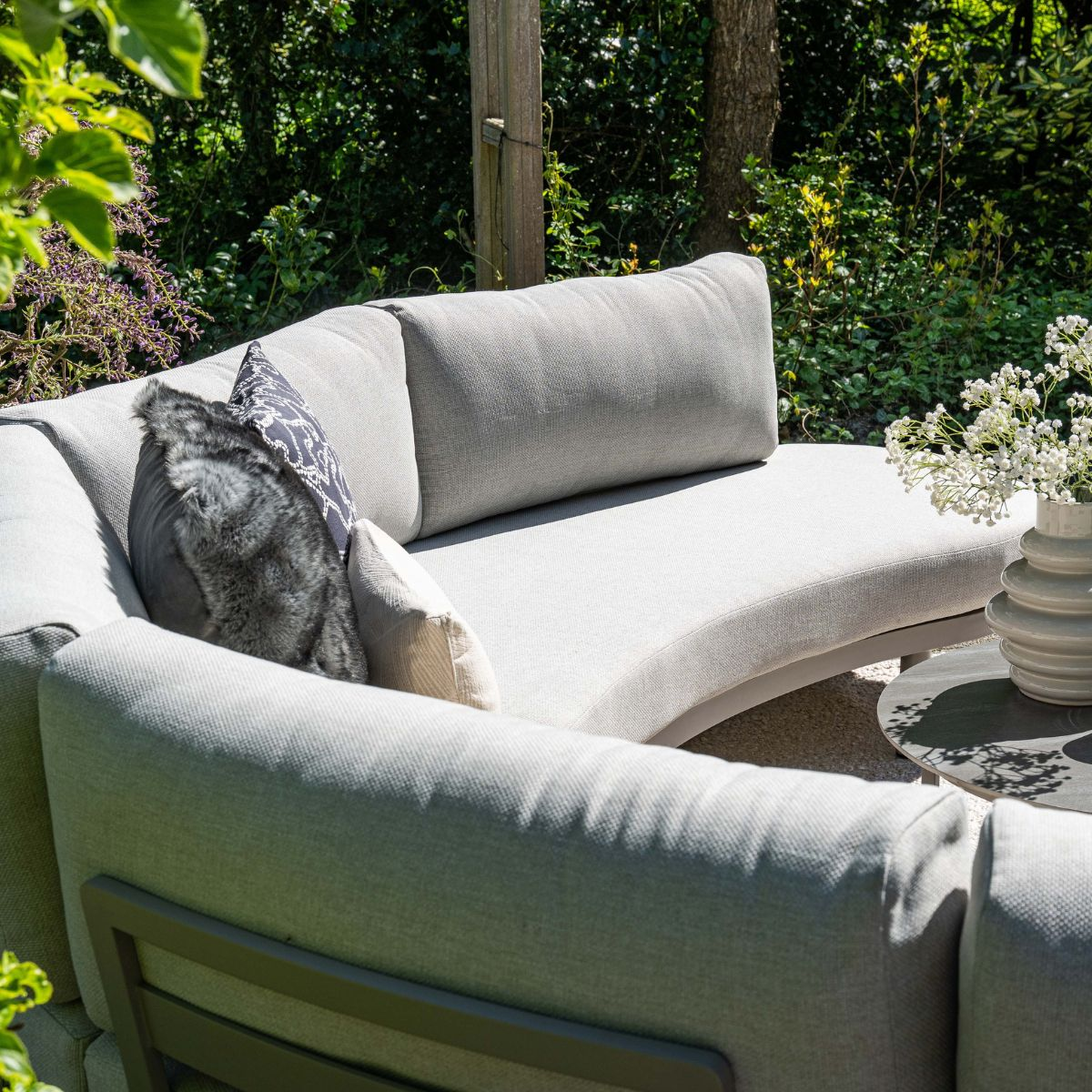 Gray outdoor lounge sofa with cushions and a vase of flowers.