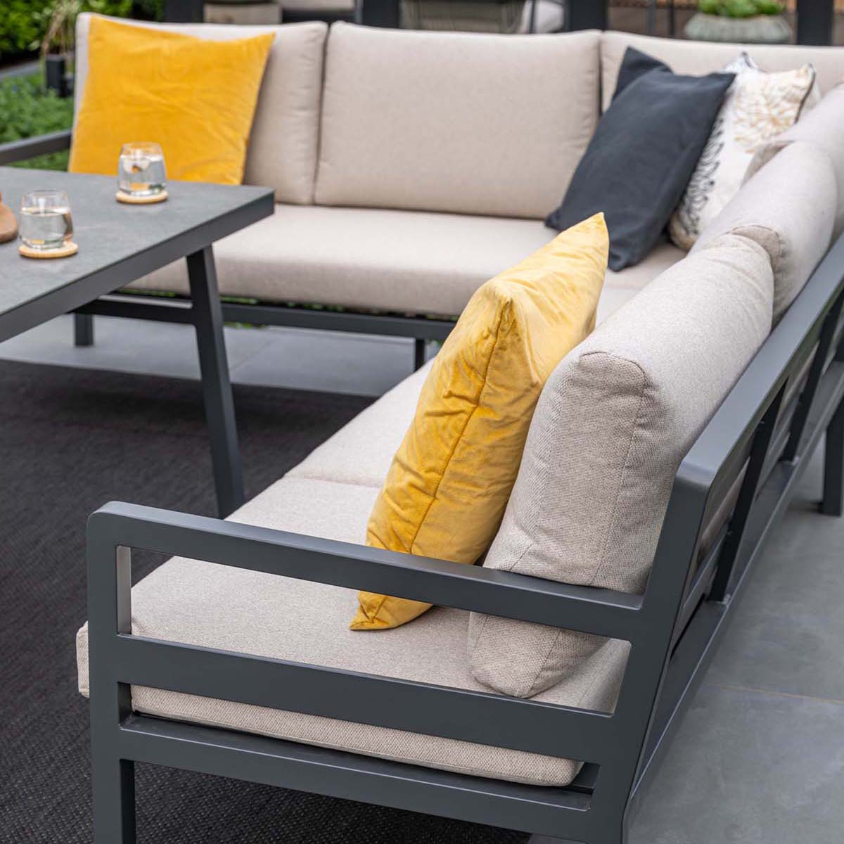 Grijze loungeset met beige en gele kussens naast een tafel.