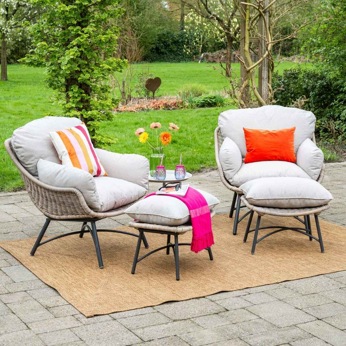 Twee buitenstoelen met kussens en plaids op een kleed in een tuin.