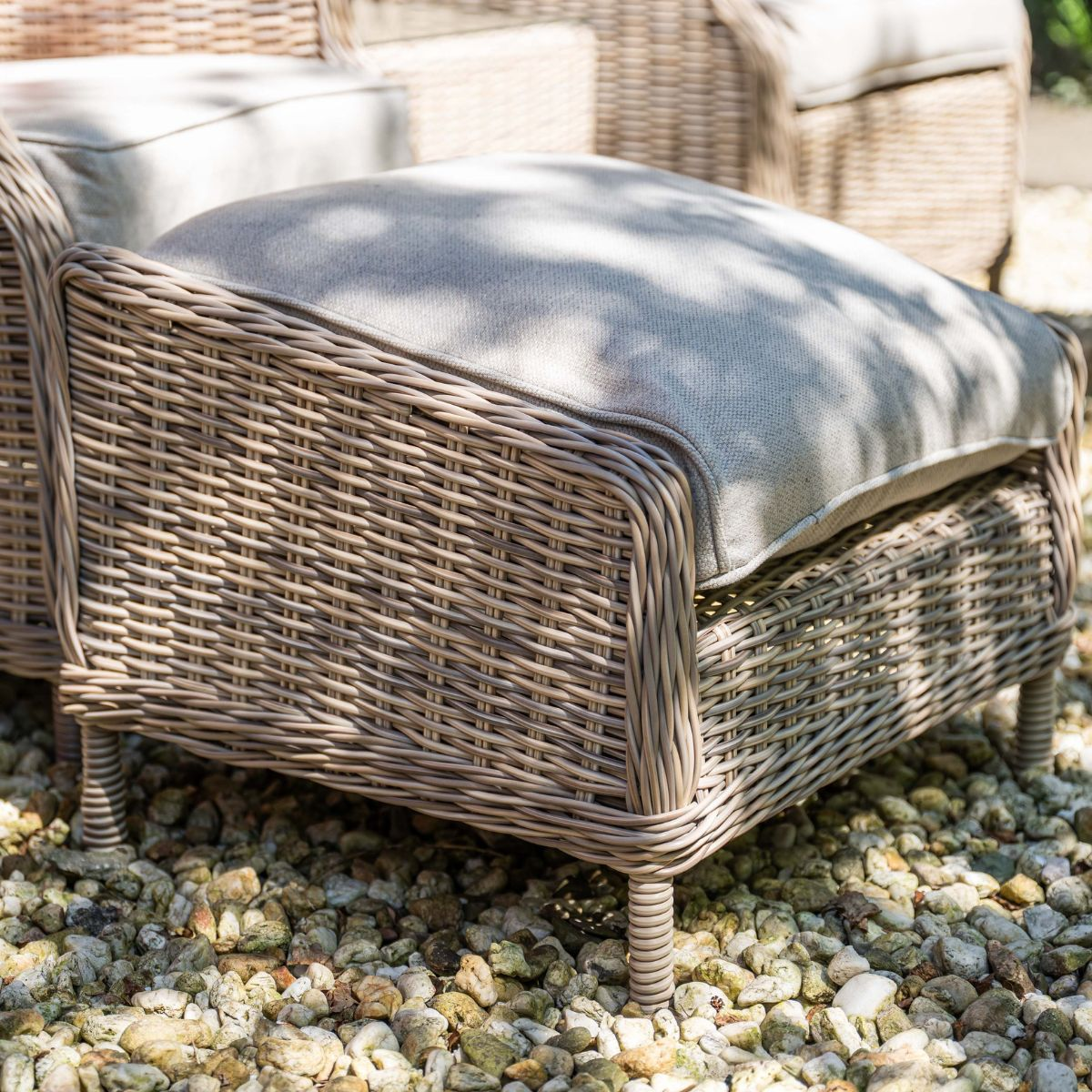 Bruine rotan fauteuil met lichtgrijs kussen op grind.