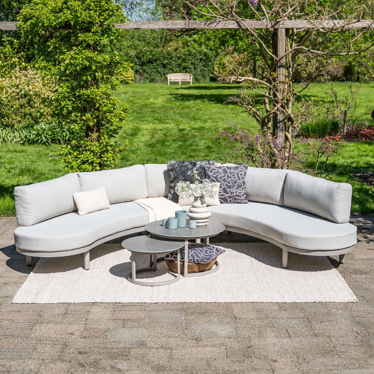 Grey sectional outdoor sofa with coffee tables and cushions on a rug.