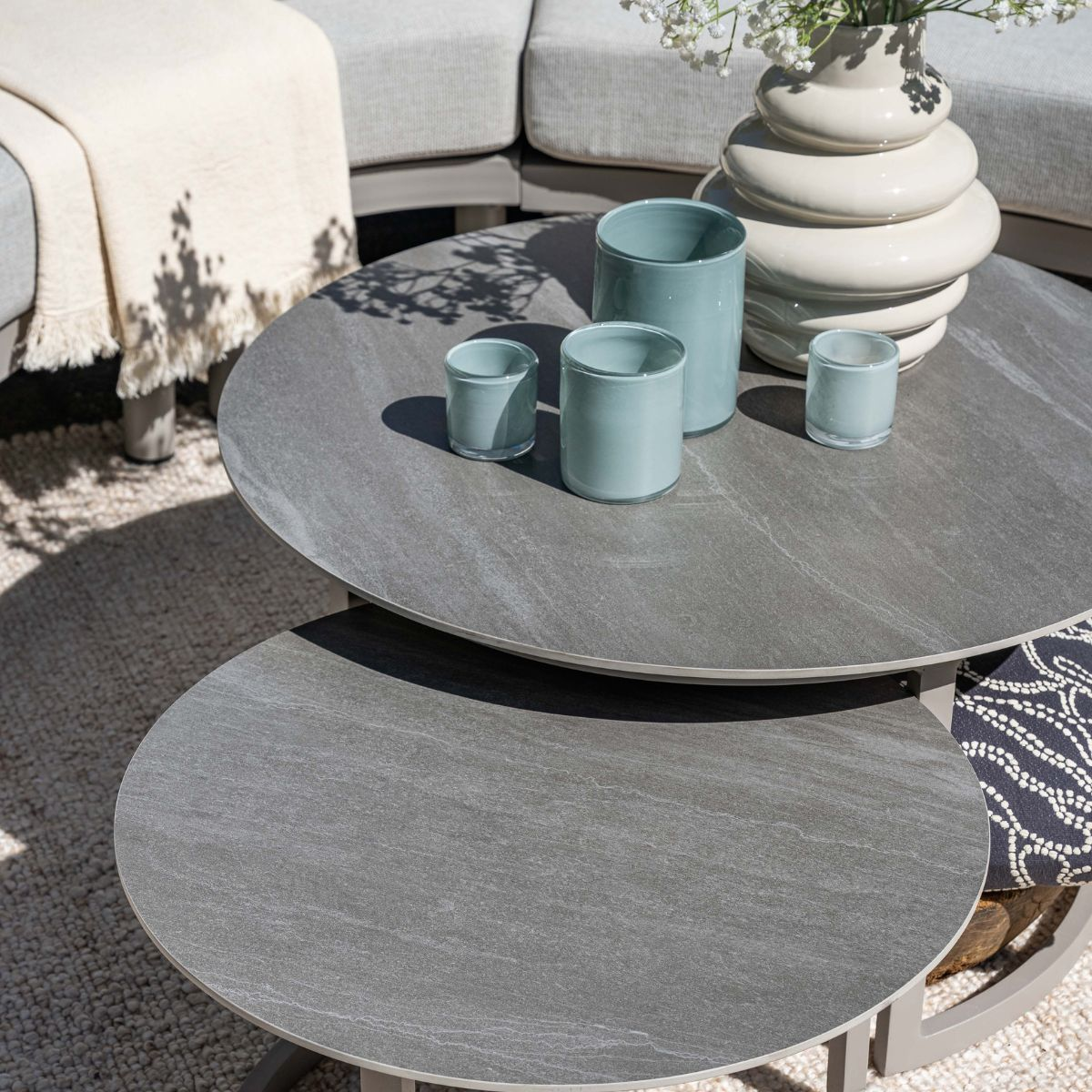 Two grey coffee tables with decor and a blanket on a rug.