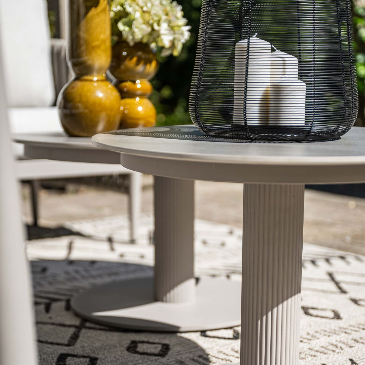 Two round outdoor tables featuring vases and candles on a rug.