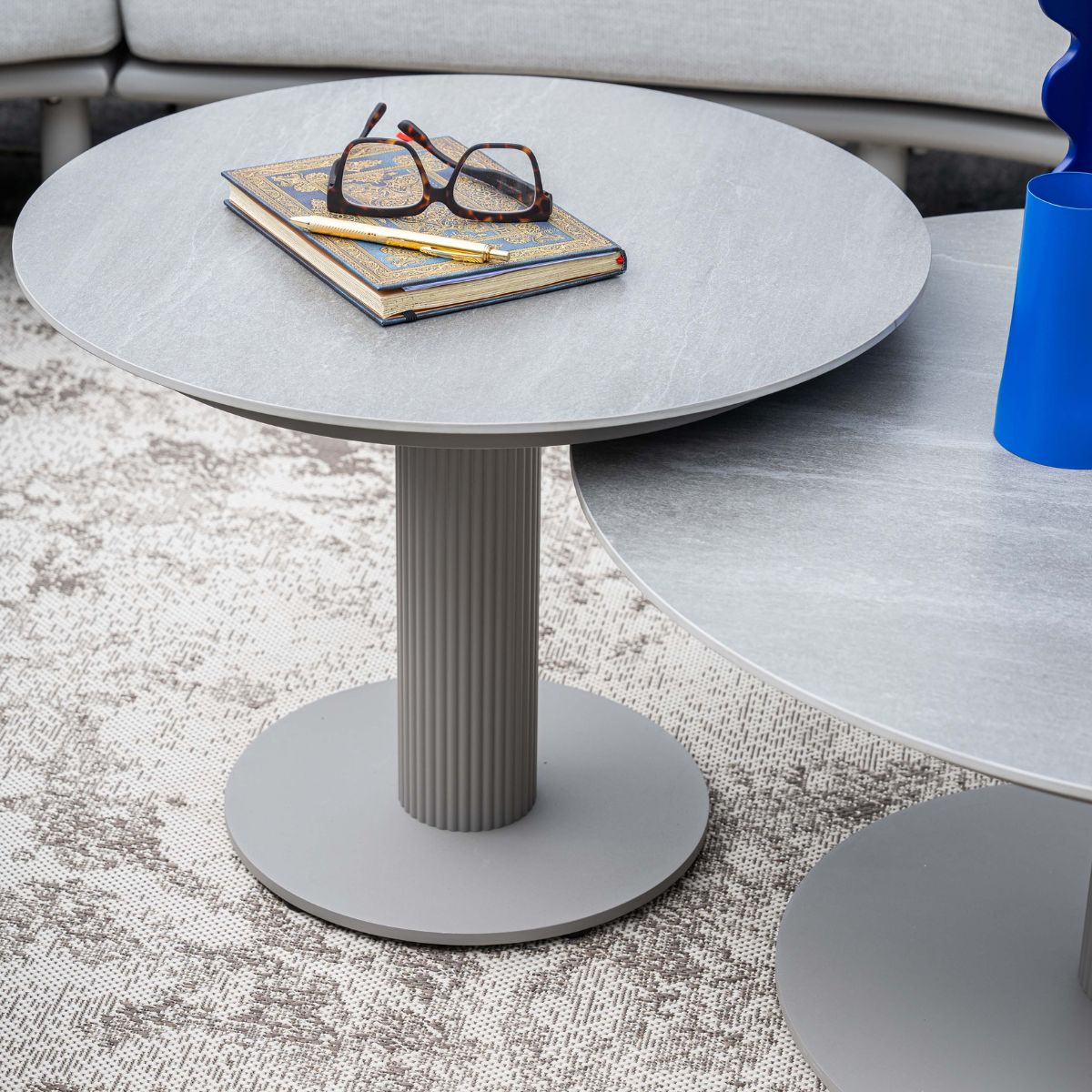 Gray side table with book, glasses, and pen. Seating in background.