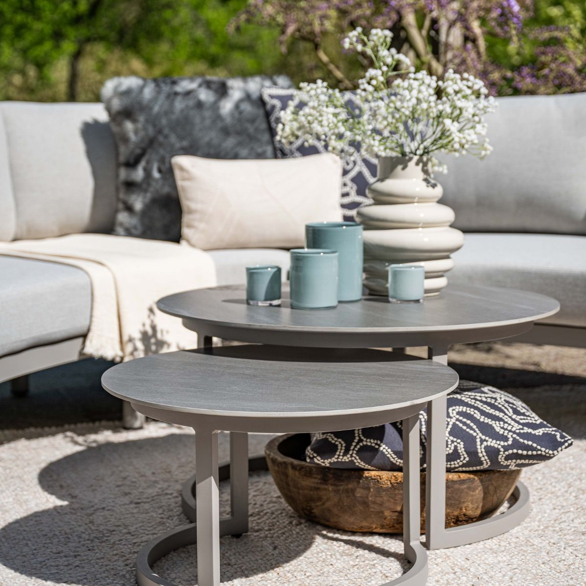 Outdoor meubelset met grijze tafels, kussens en bloemen in vaas.