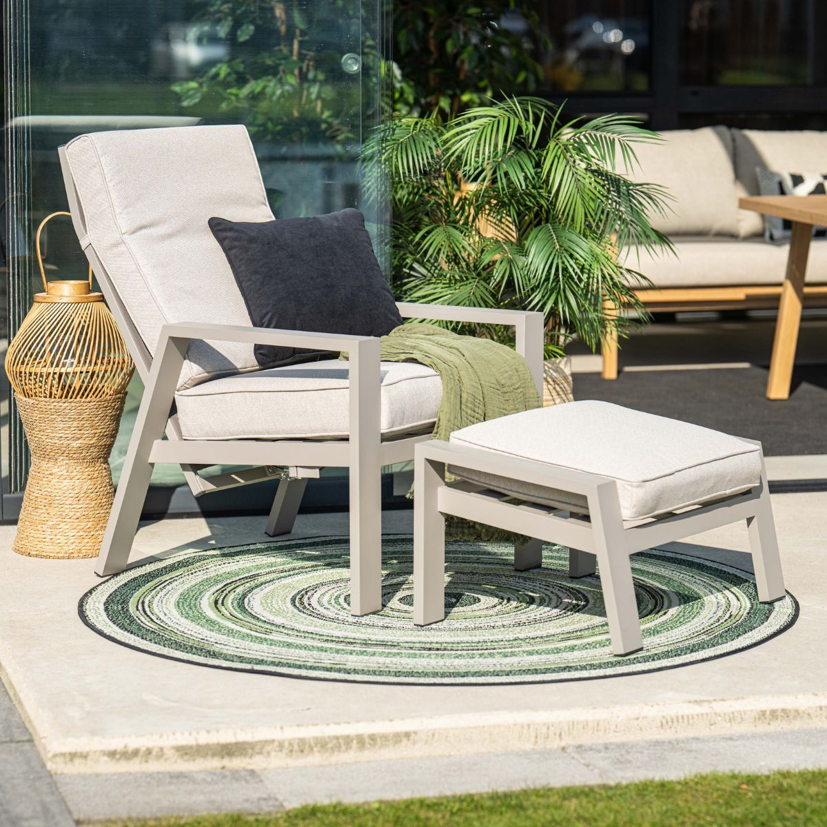 Een lichte fauteuil met een hocker en deken op een ronde mat.