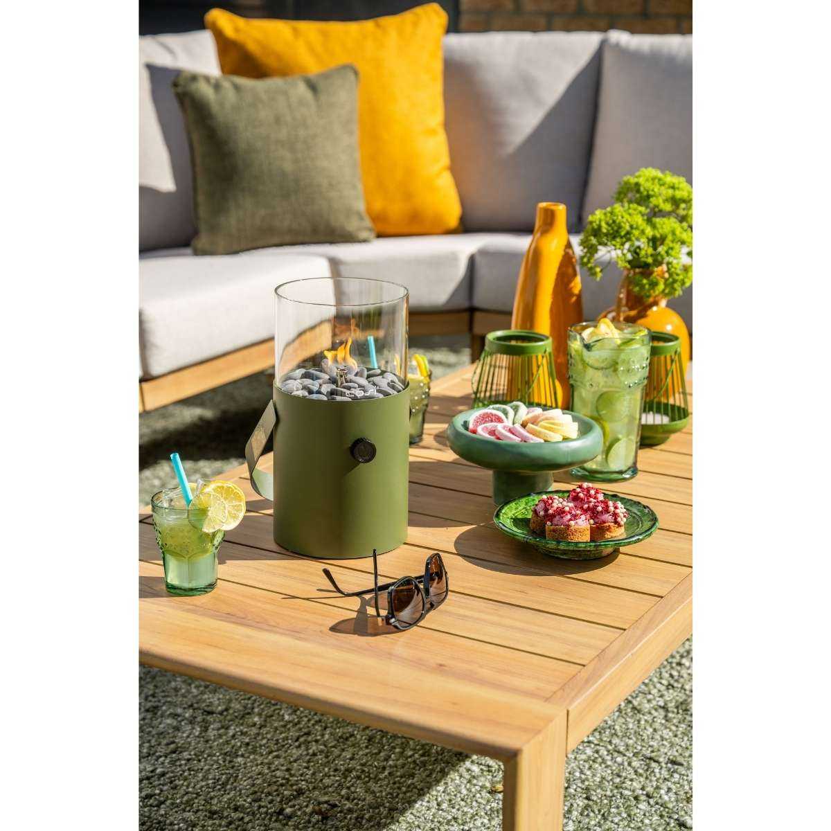 Een buitentafel met een groene vuurkorf, drankjes en snacks.