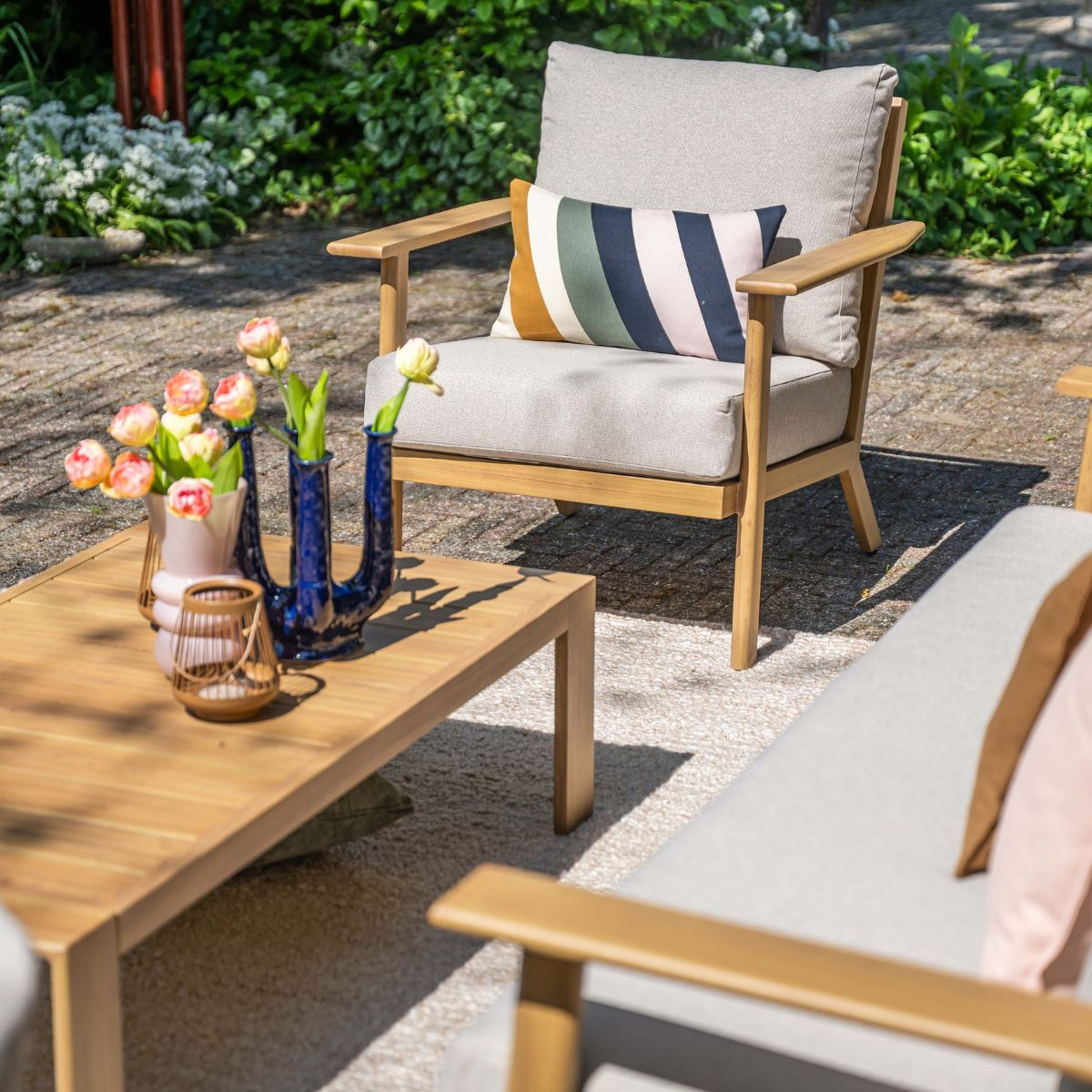 Outdoor furniture with cushions and flowers on a wooden table.