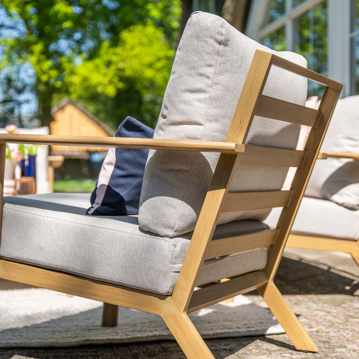 A comfortable wooden chair with gray cushions and blue accents outdoors.