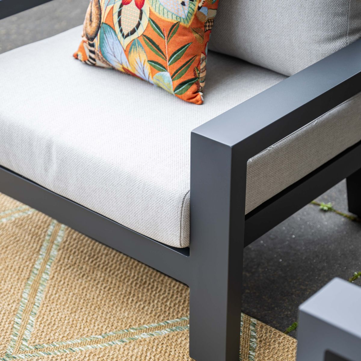 Grijze fauteuil met oranje kussen met vogelmotief op vloerkleed.