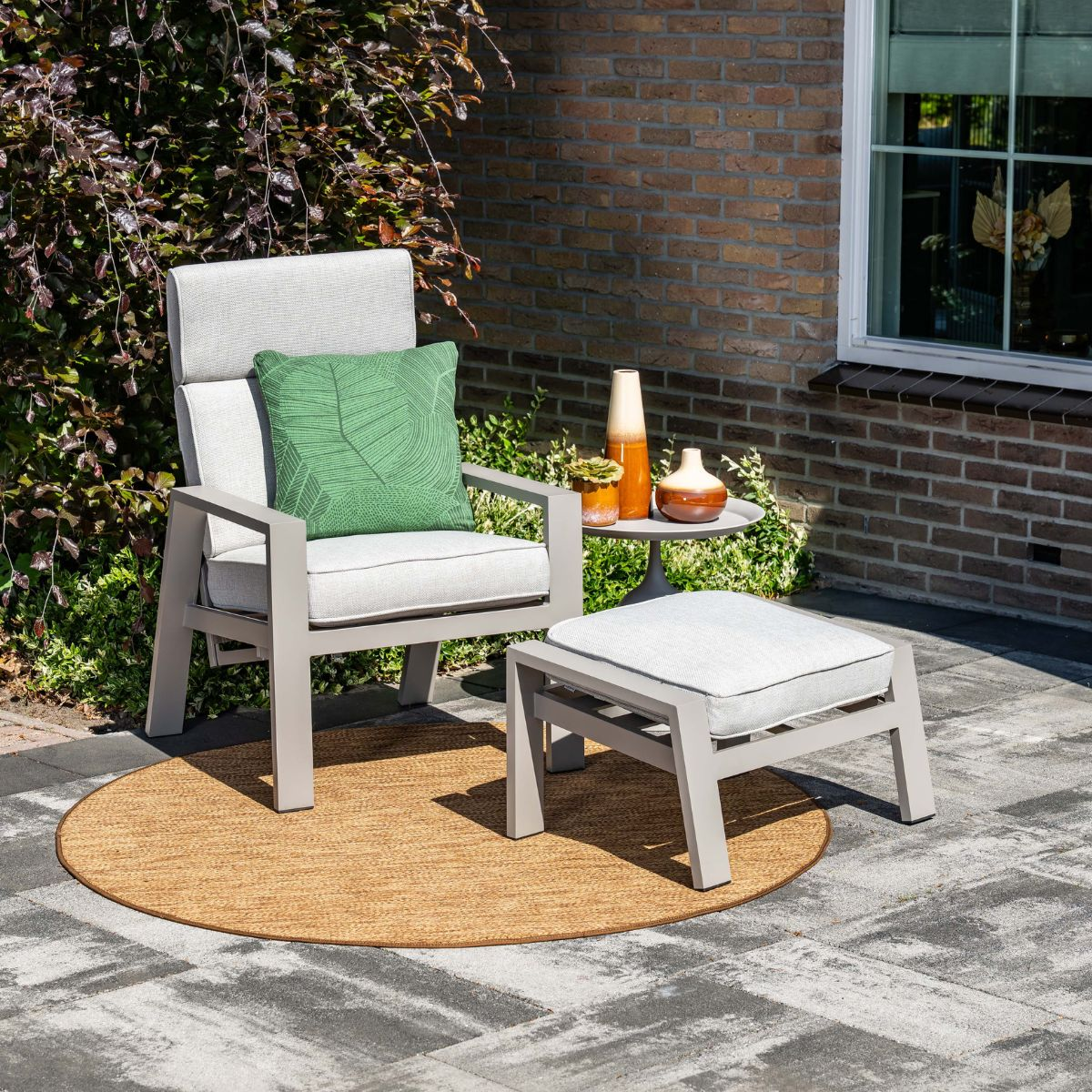 Een grijze fauteuil met groen kussen op een rond buitenkleed.