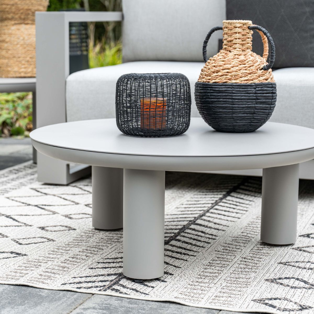 Gray coffee table with candle holder and basket vase, sofa in background.