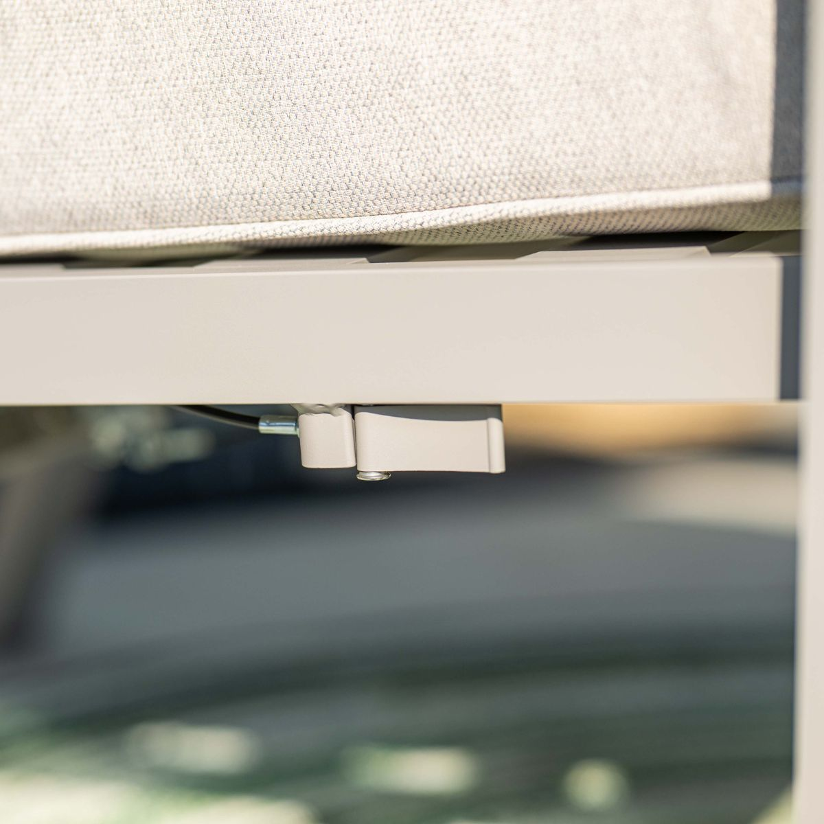 Close-up van een lichtgekleurd stoffen kussen op een witte metalen structuur met mechanisme.