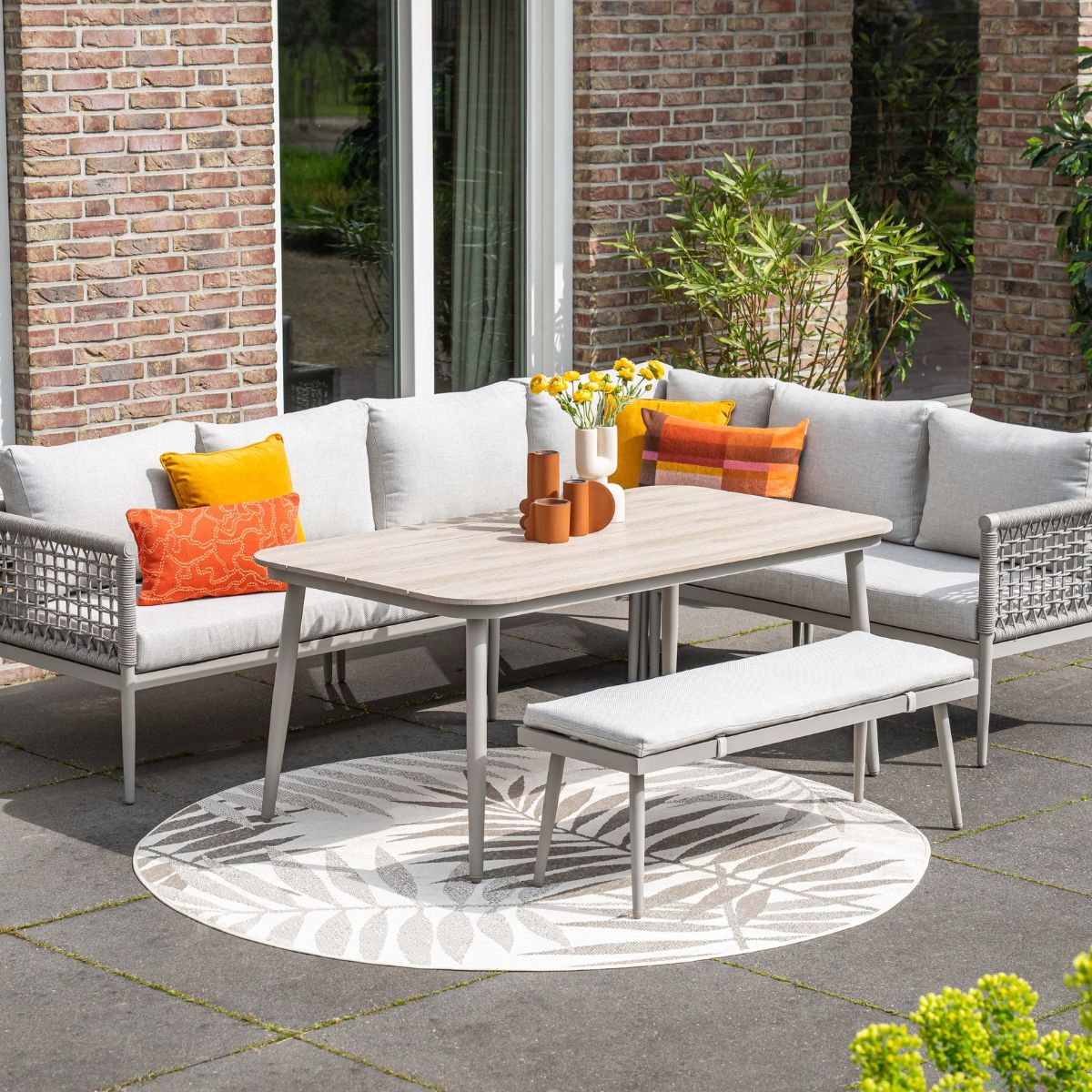 Grijze lounge set met tafel en bank op een ronde vloerkleed met bladmotief.