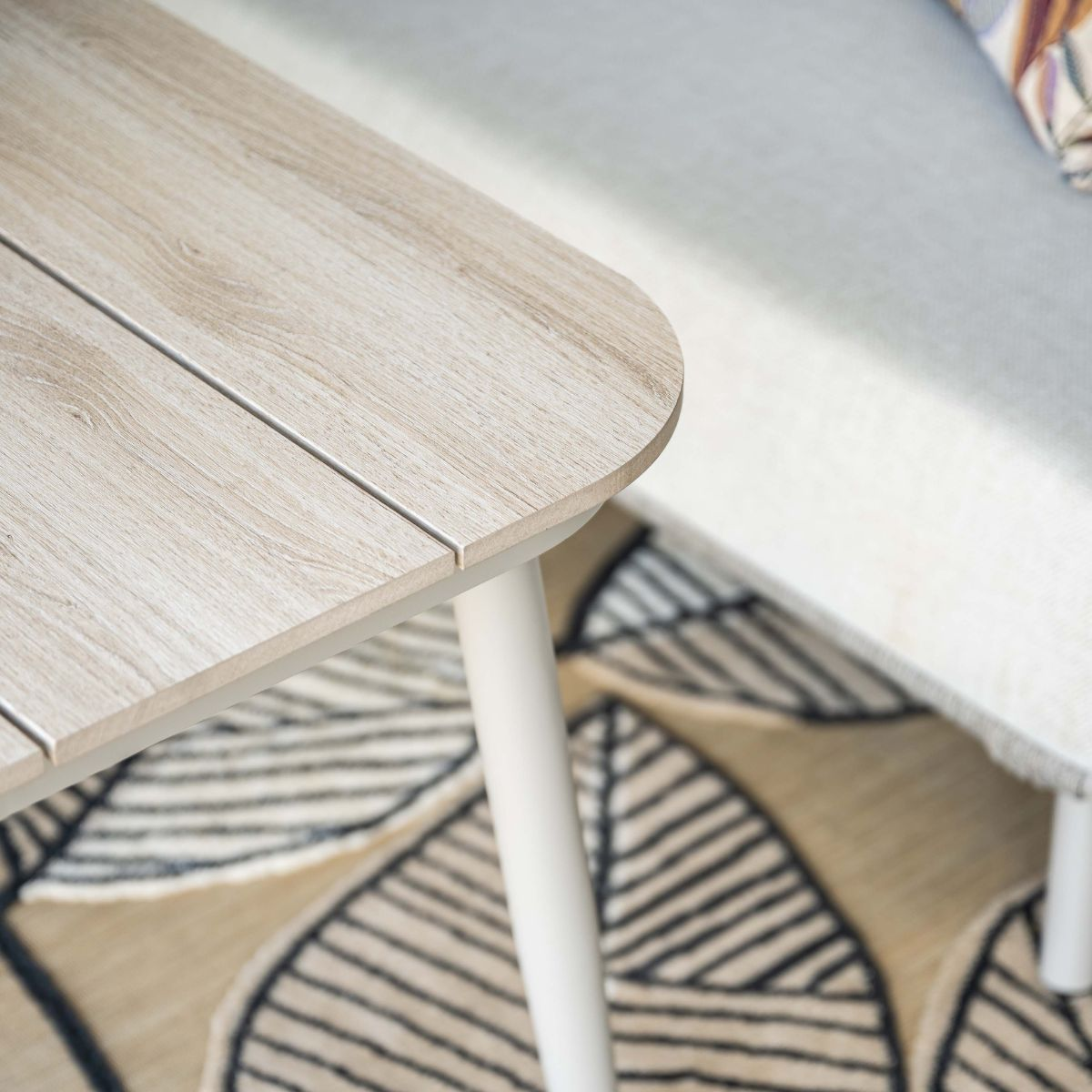 Licht houten meubel met witte poten op een vloerkleed met bladmotief.