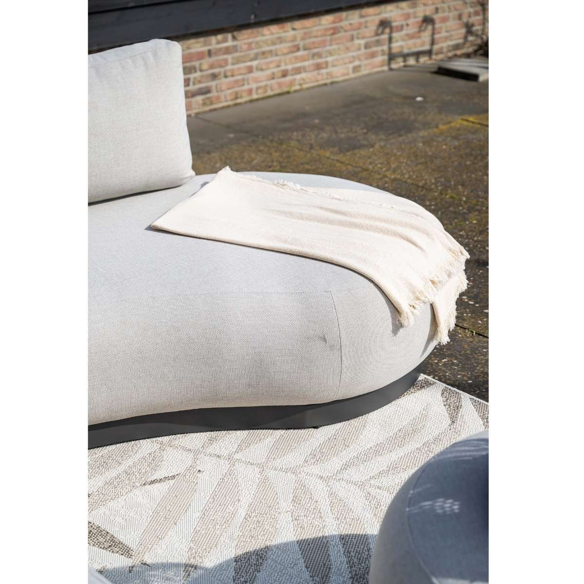 Een lichtgrijze buitensofa met een beige plaid op een patio.