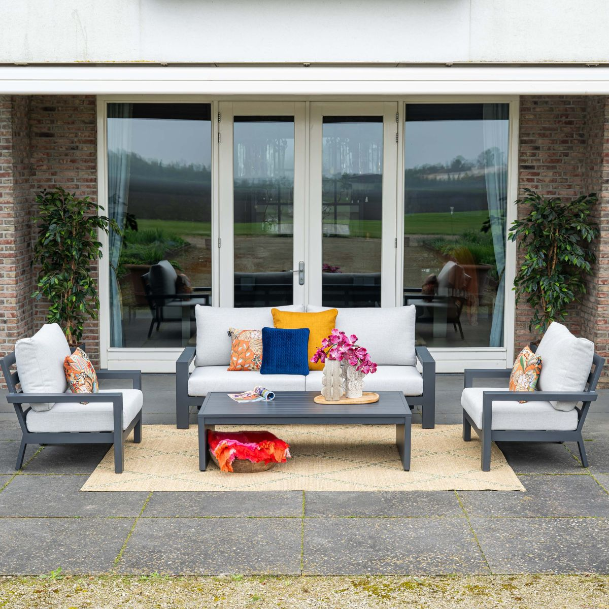 Gray outdoor furniture set with sofa, armchairs, coffee table and cushions on a rug.