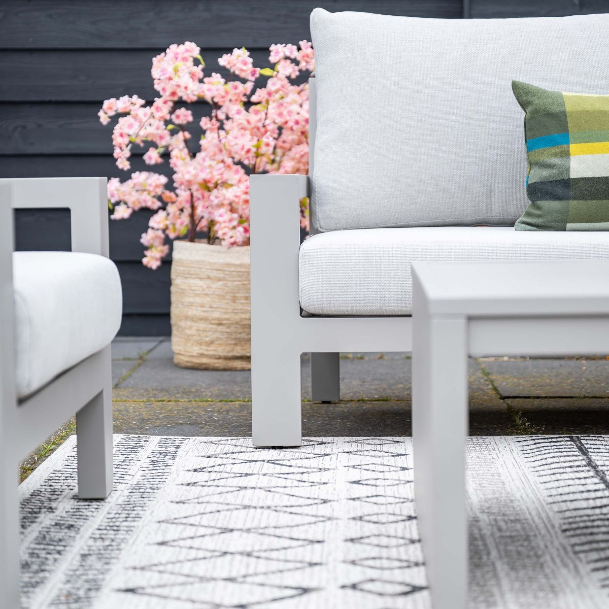 Gray outdoor furniture with white cushions, pink flowers, and rug.