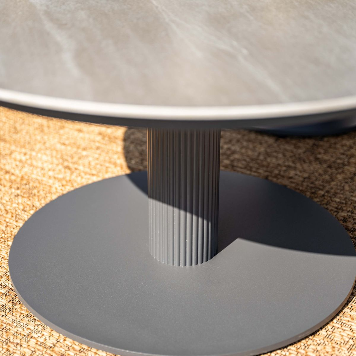 A grey table base with a fluted pedestal on a woven mat.