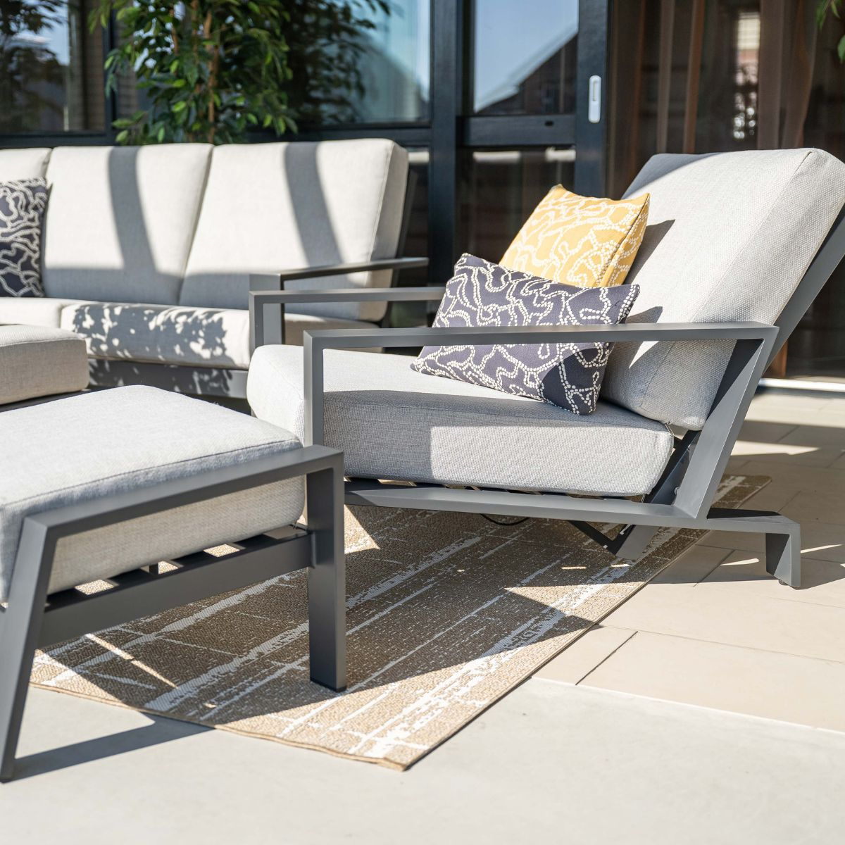 Gray outdoor lounge furniture with cushions on a patio, with sun and shadows.