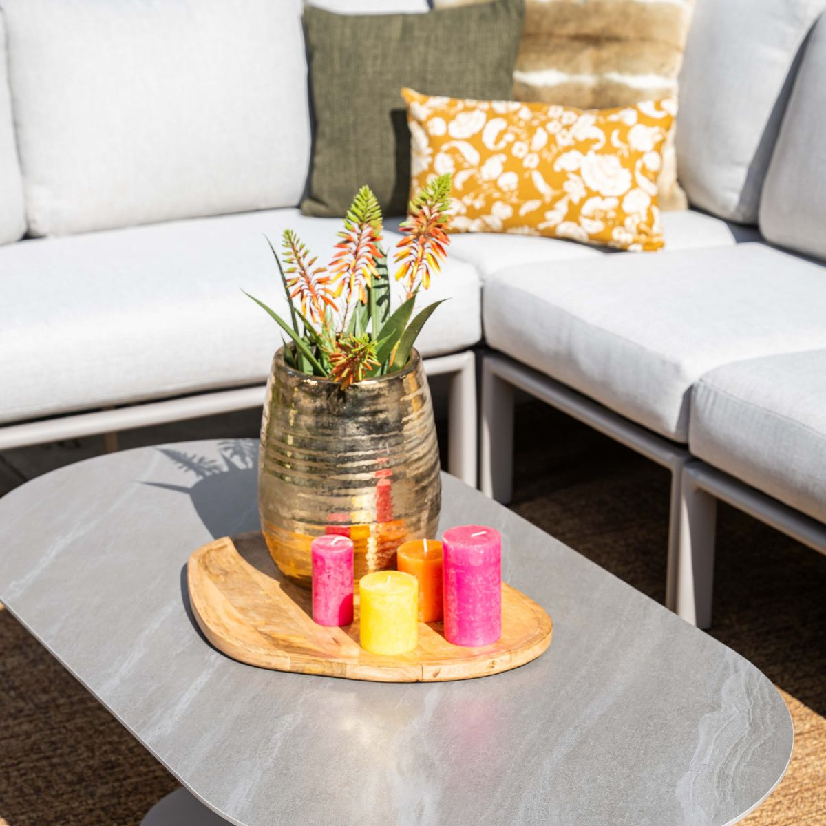 Grijze tafel met gouden pot, bloemen en kleurrijke kaarsen voor een bank.
