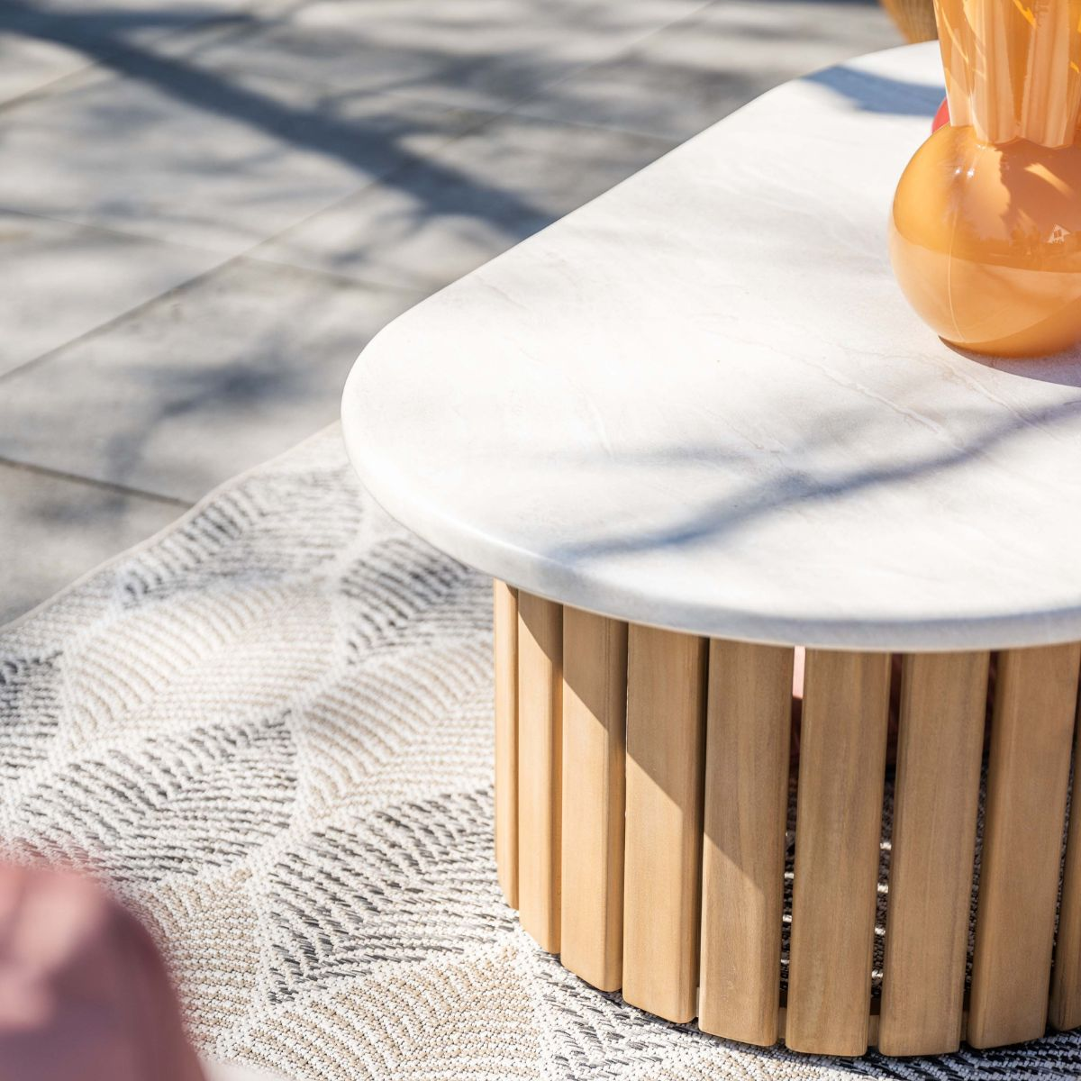 A round coffee table with a marble top and wooden base on a patterned rug.