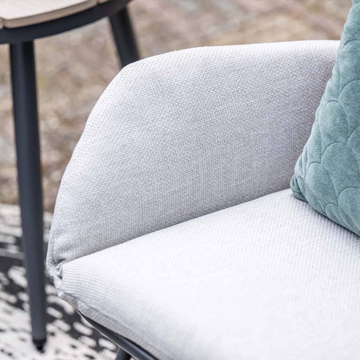 Een grijze fauteuil met een teal kussen en een tafel op de achtergrond.