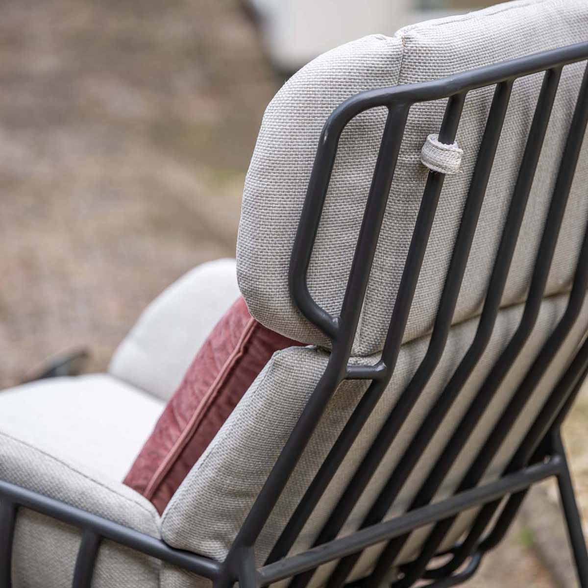 Een grijze fauteuil met metalen frame en een rood kussen buiten.
