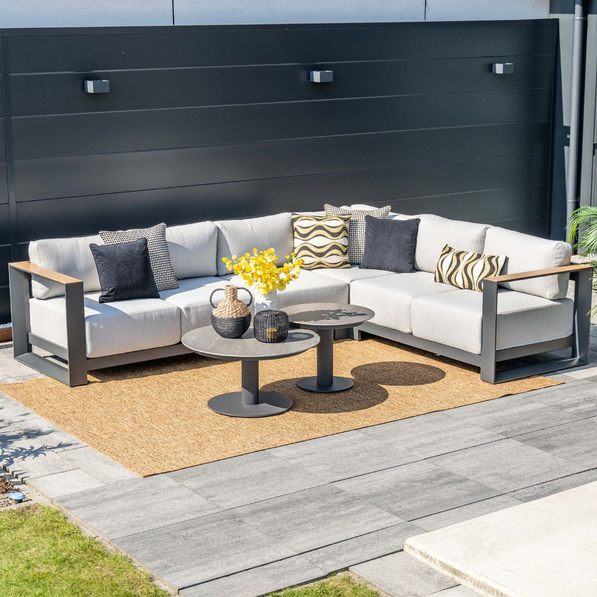 Gray sectional sofa with cushions and coffee tables on rug in front of dark wall.