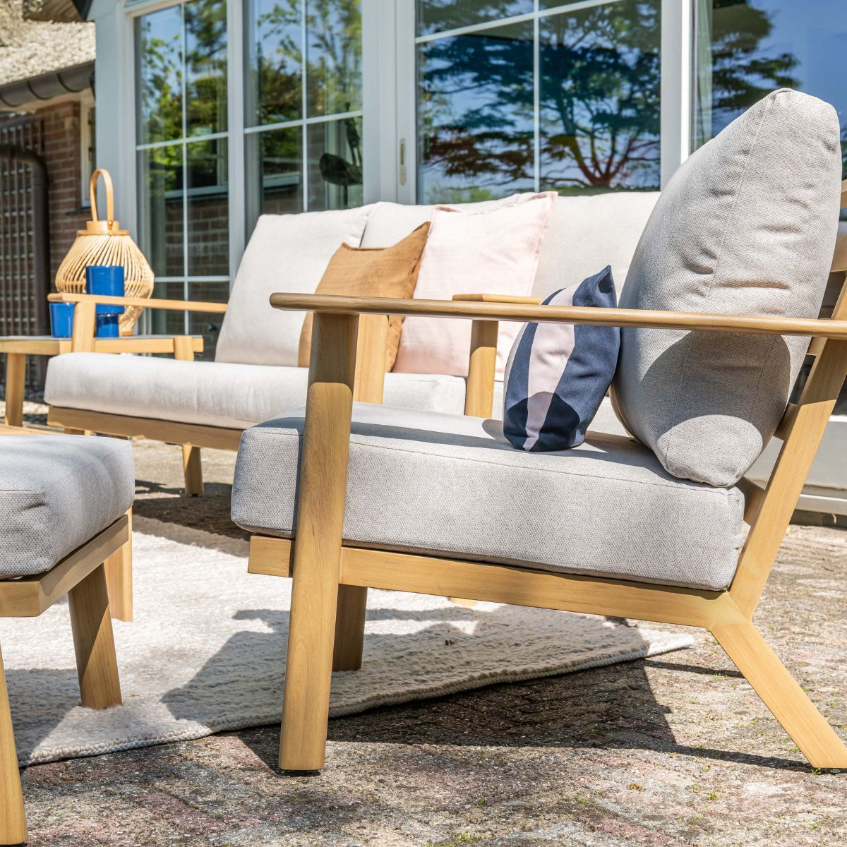 Wooden outdoor furniture with cushions on a patio with windows in the background.