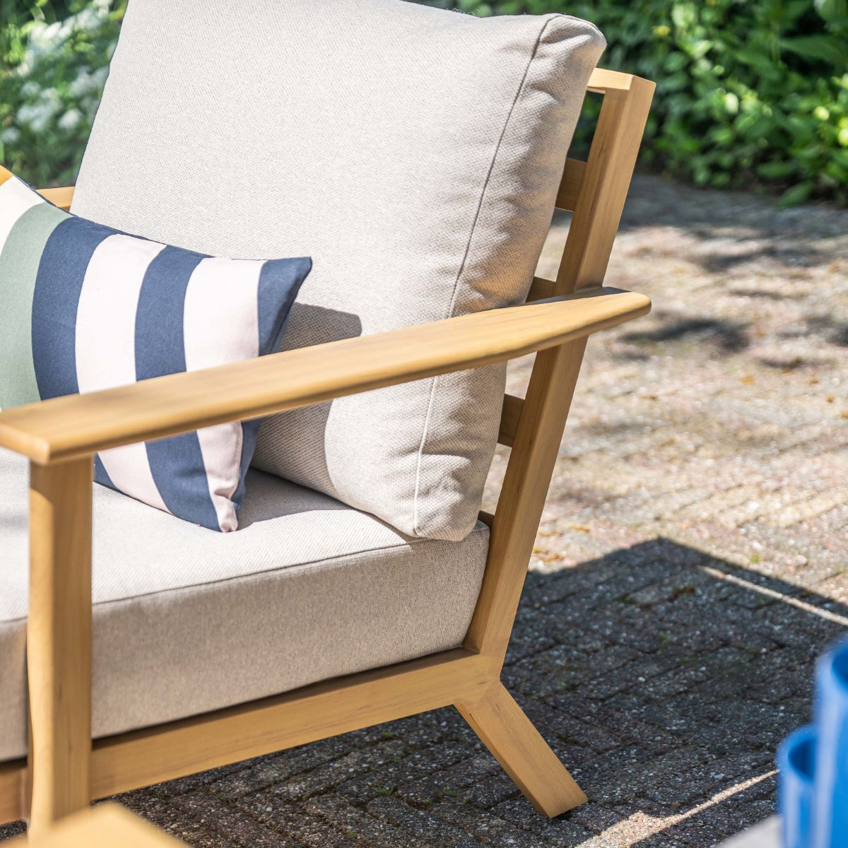 A wooden chair with light cushions and a striped pillow outdoors.
