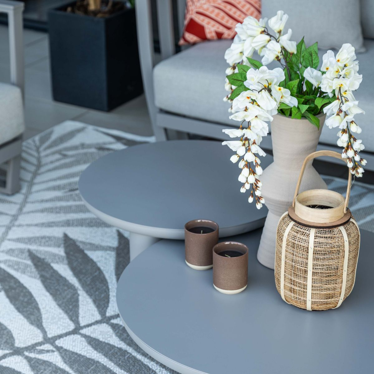 Twee grijze tafels met kaarsen, vaas met witte bloemen en lantaarn.
