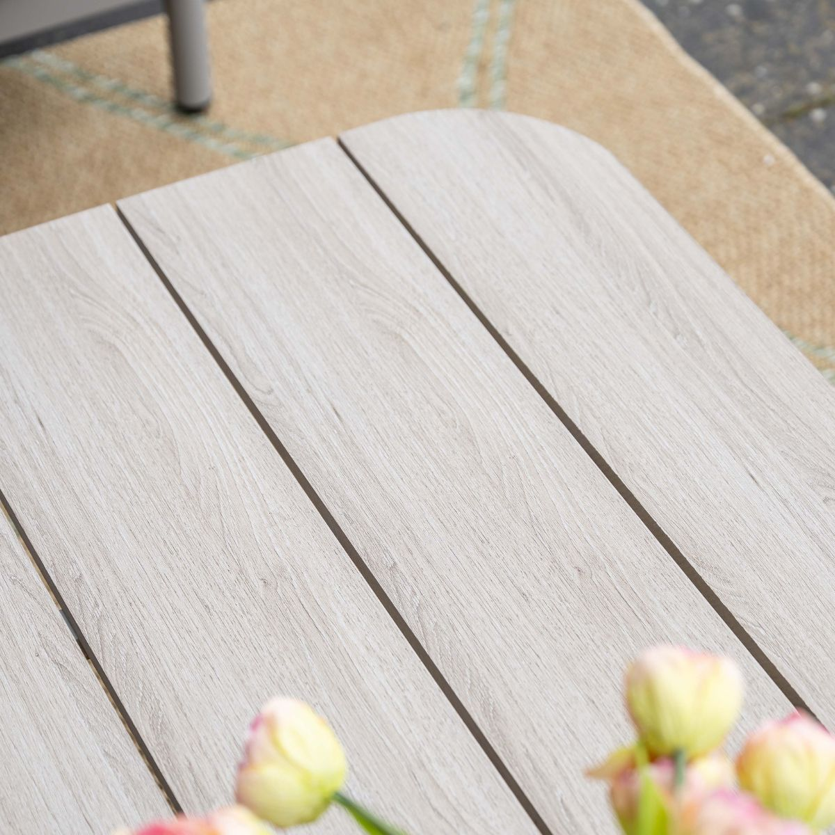 Wooden tabletop with tulips and a rug in the background.