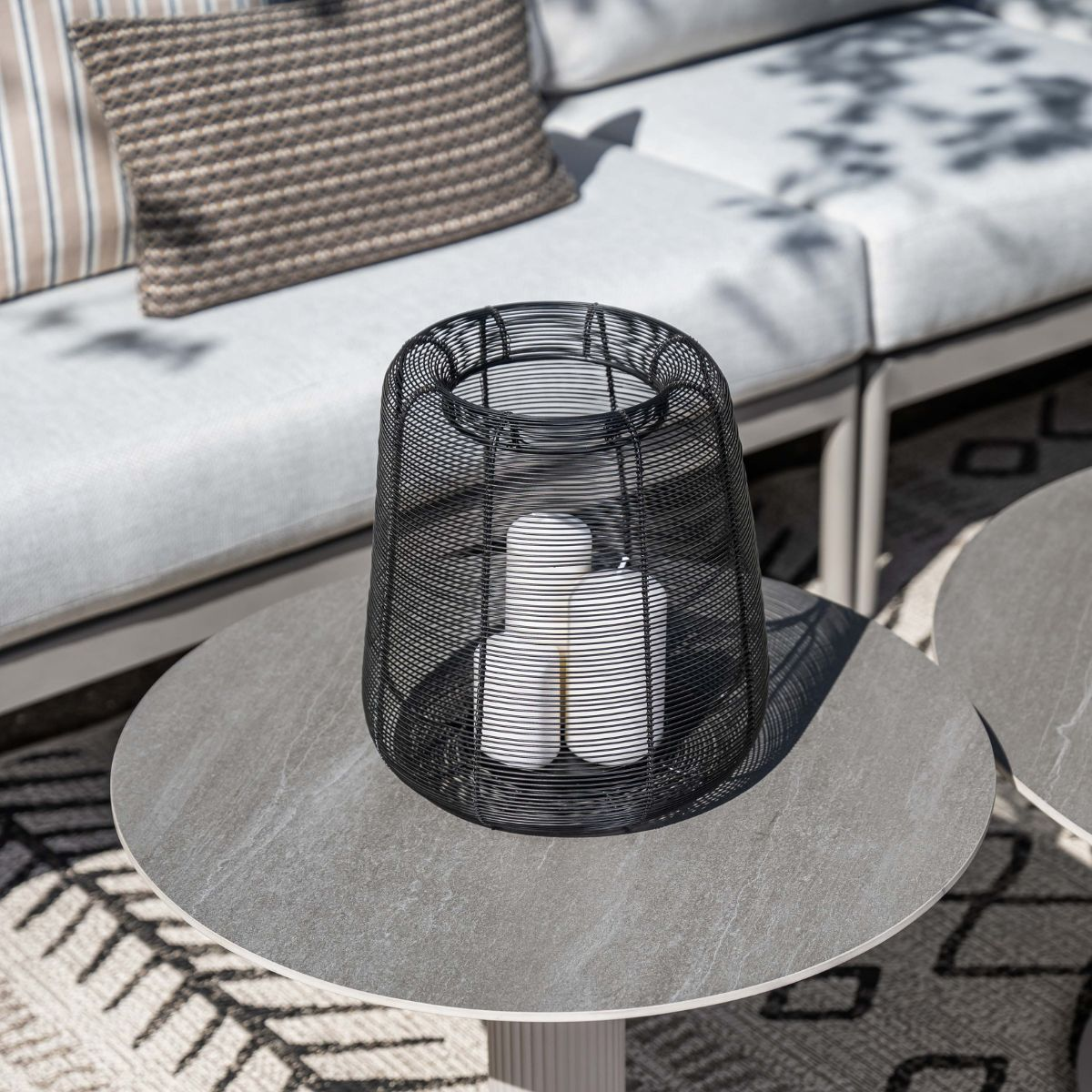 Black wire lantern with white candles on a round table.