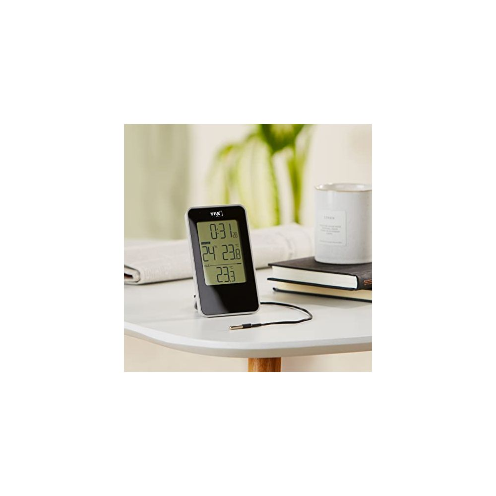 Digitales Thermometer auf Tisch mit Büchern und Kerze. Zeigt 0:31, 24 und 23.3 Grad.