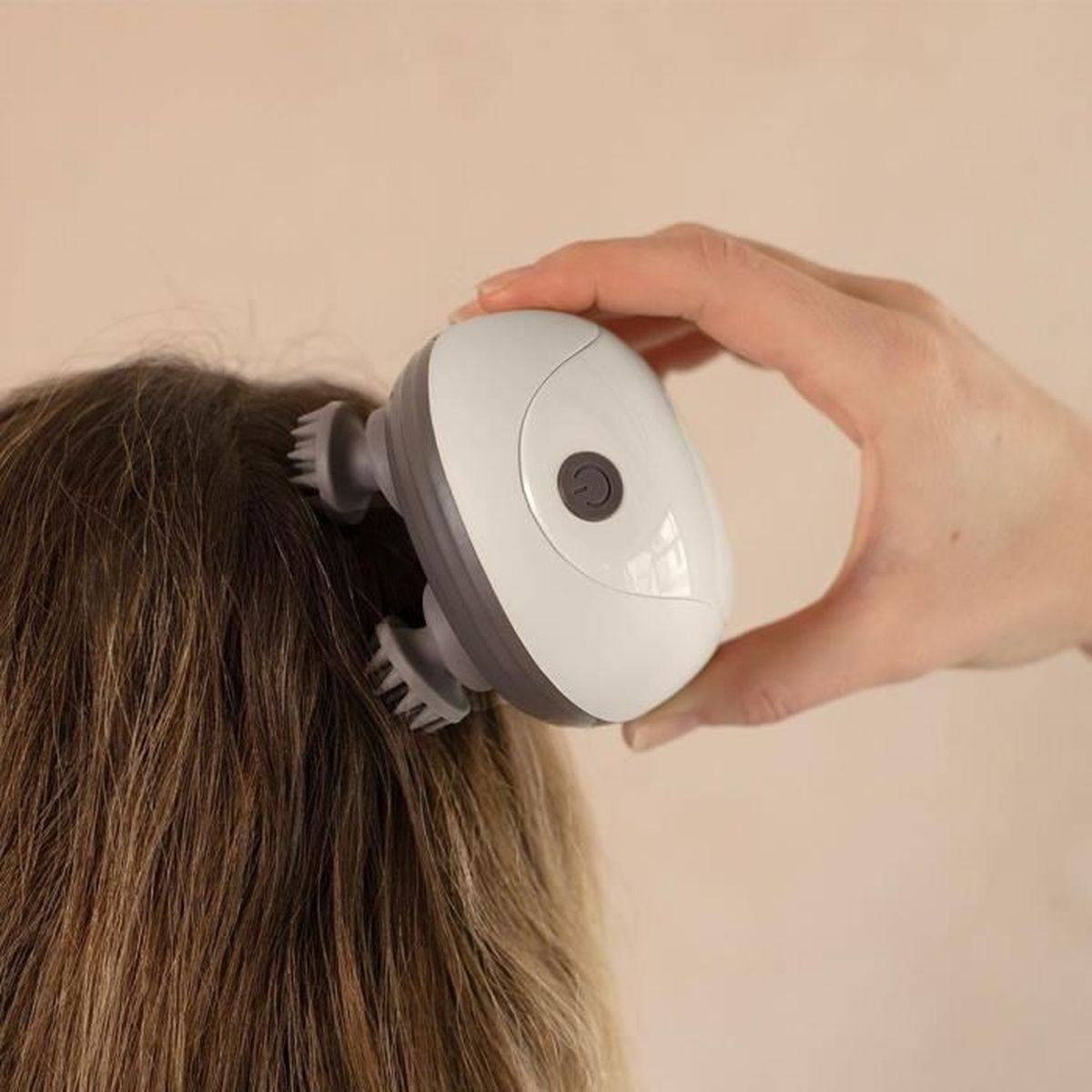 Mano che tiene un massaggiatore bianco sulla testa di persona con capelli castani.