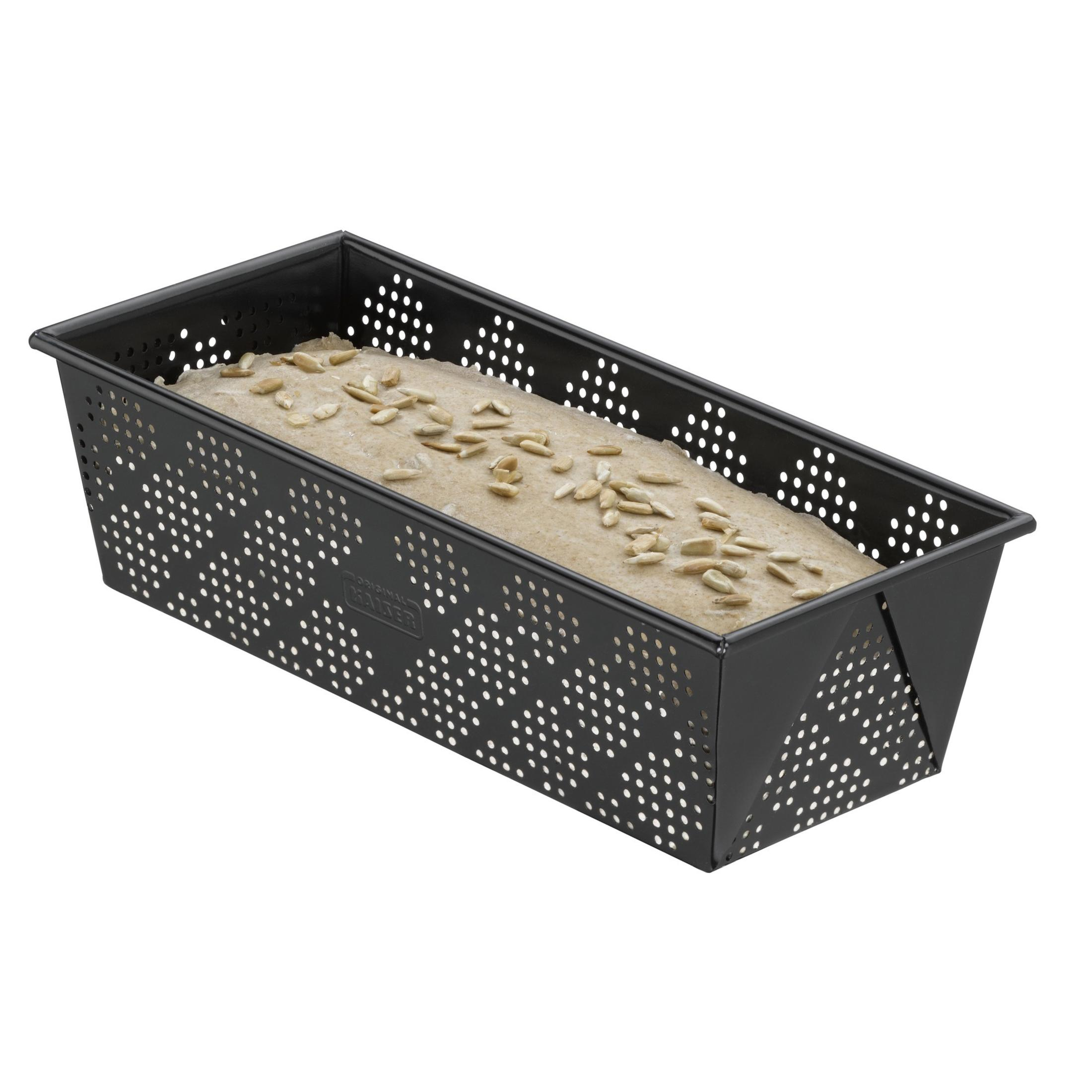 Ein rechteckiger, perforierter Brotbackform mit ungebackenem Teig und Sonnenblumenkernen.