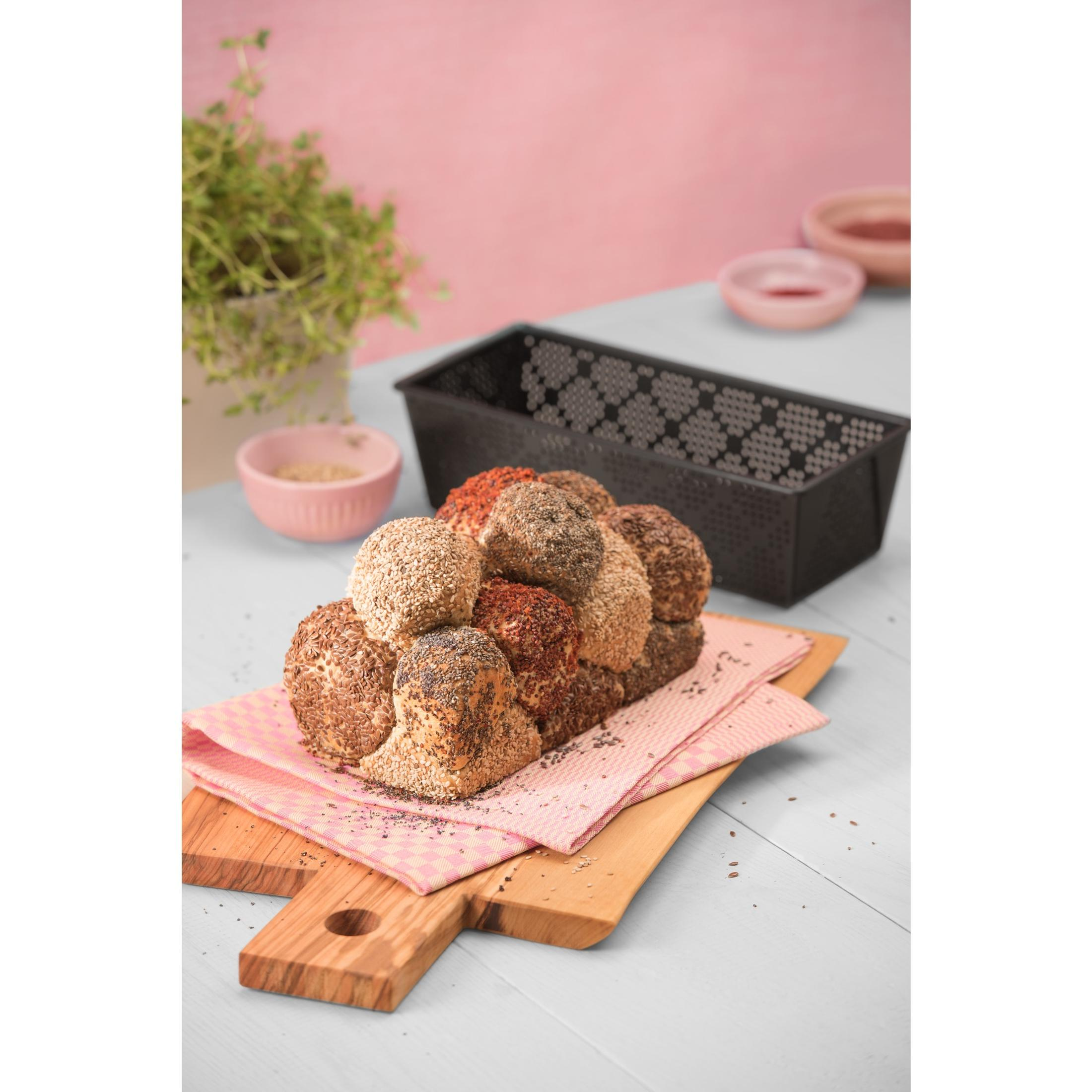 Brotlaib mit Sesam und Mohn auf Holzbrett mit rosa Tuch.