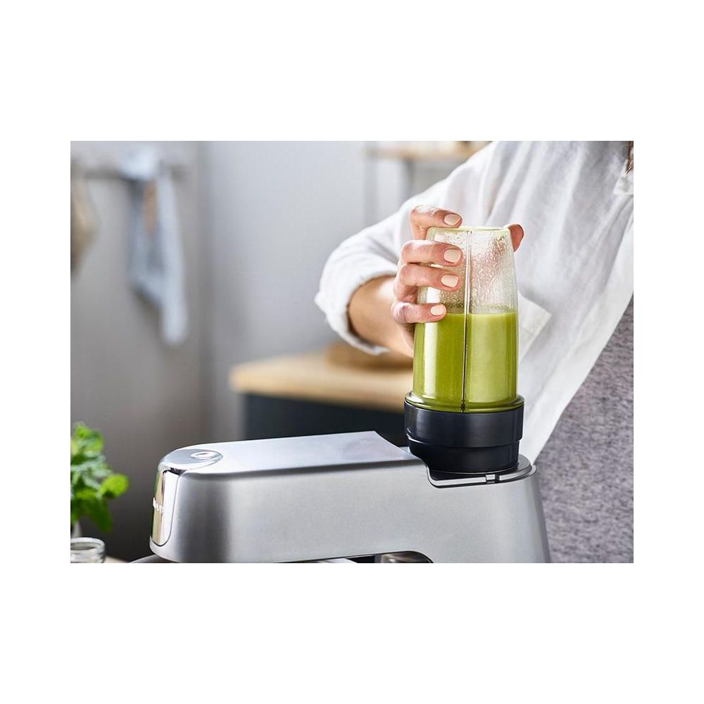 Eine Person mixt einen grünen Smoothie in einem silbernen Mixer in der Küche.