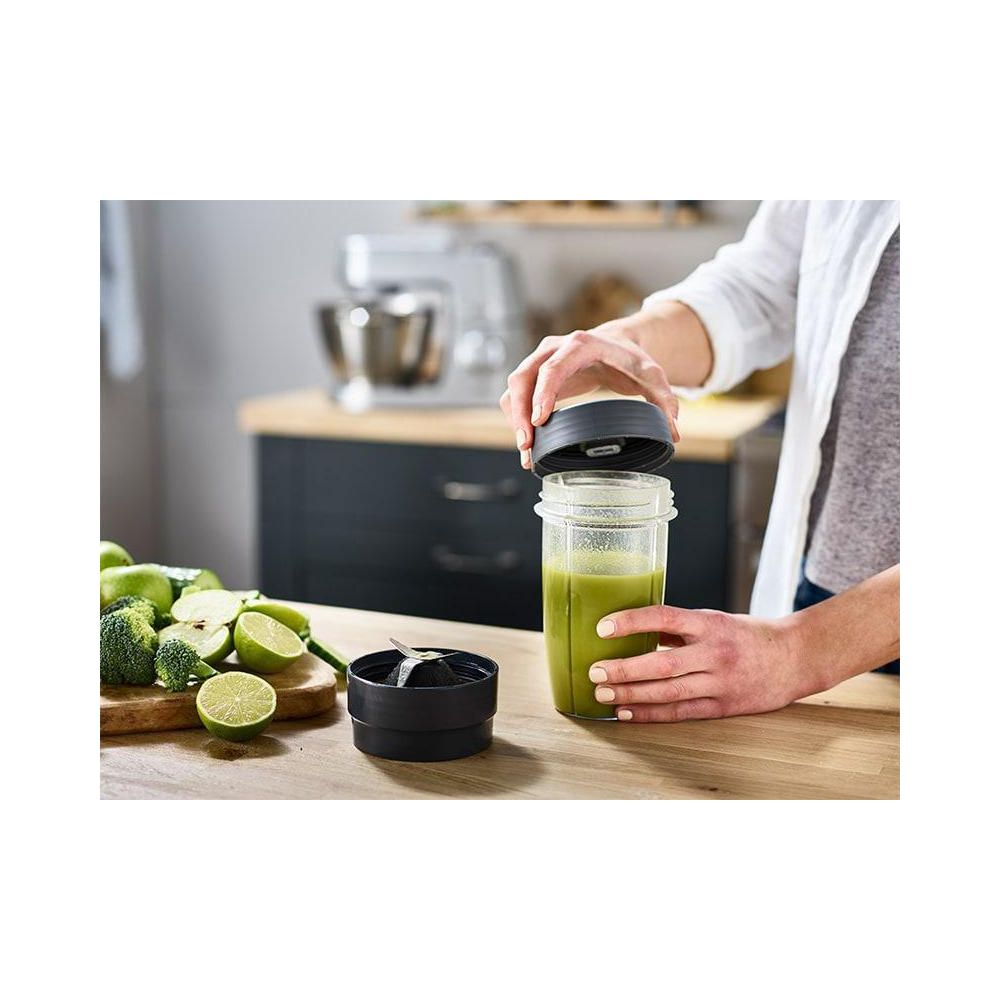 Eine Person schließt einen Mixerbecher mit grünem Smoothie. Zutaten liegen daneben.