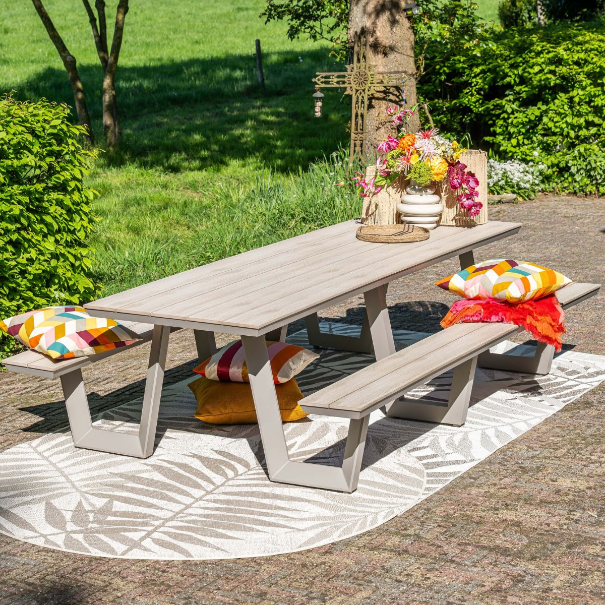 An outdoor wooden table with benches, decorated with colorful cushions and flowers.