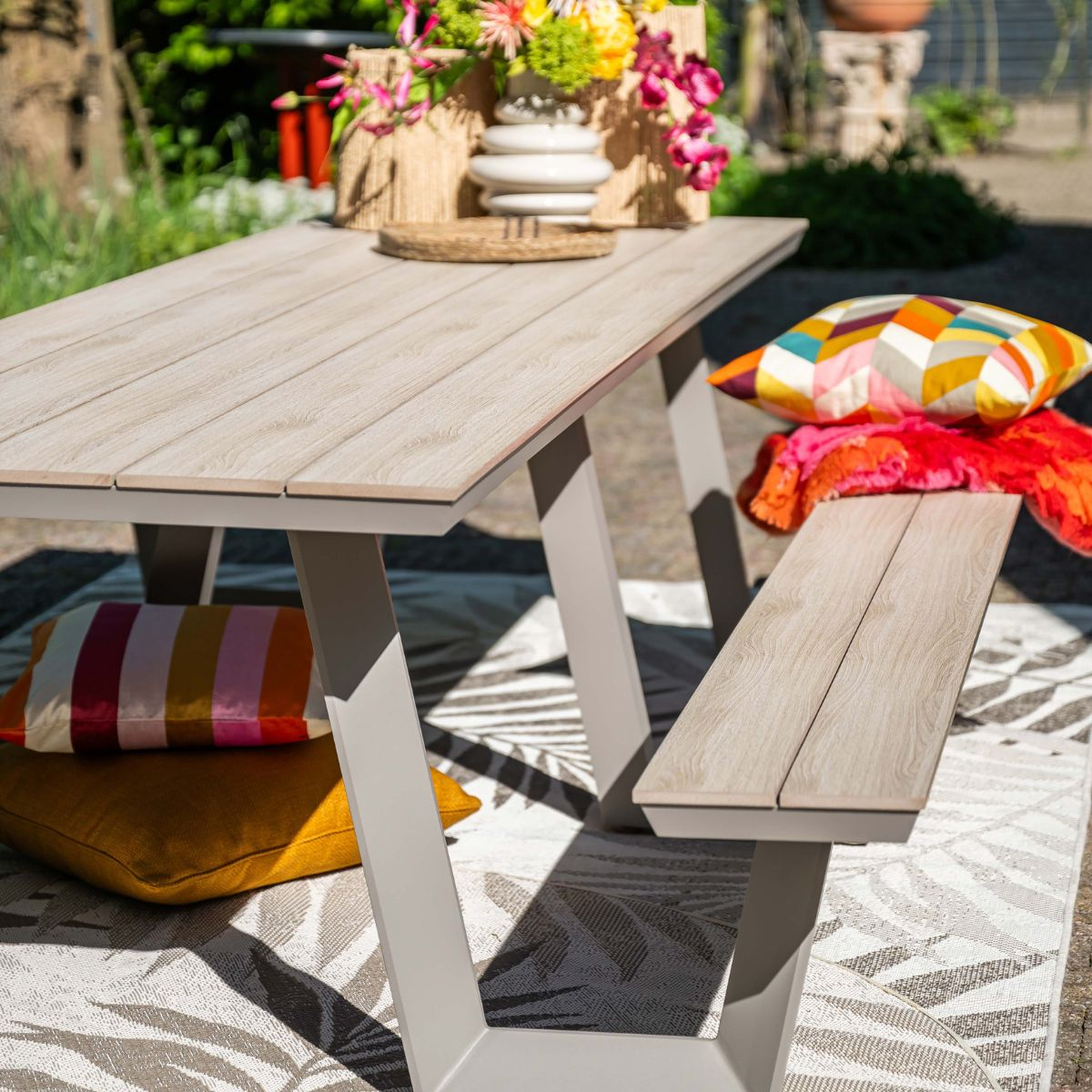 A wooden table and bench with colorful cushions outdoors.