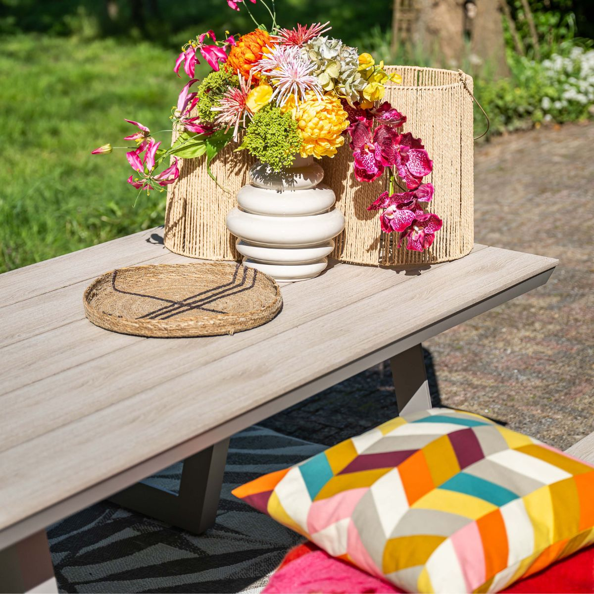 A colorful flower arrangement in a vase on a wooden table with cushions.