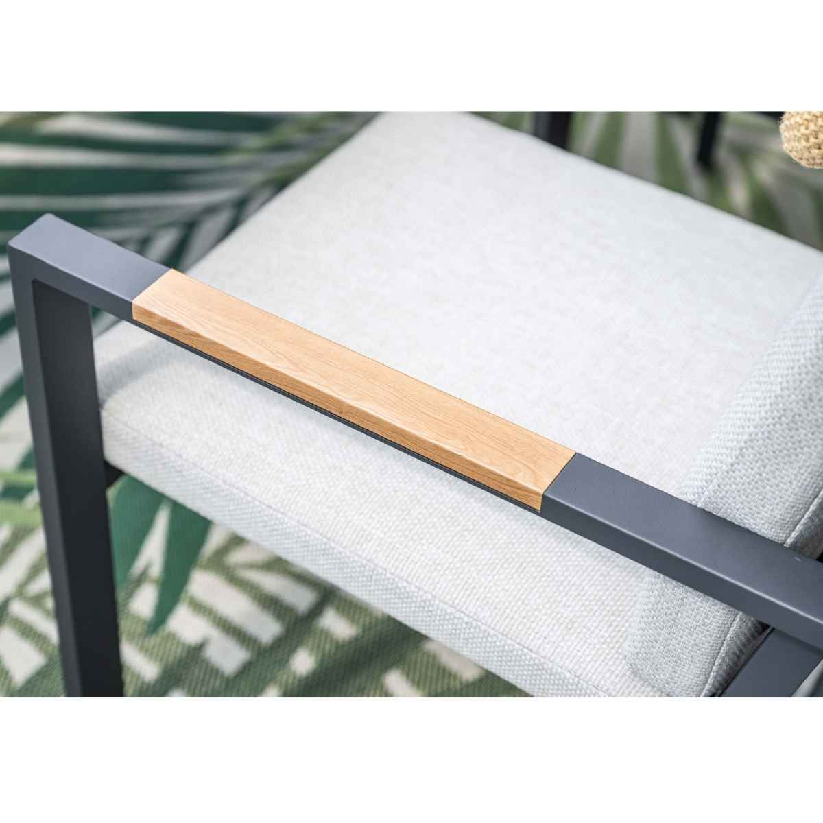 Grijze stoel met houten armleuning en lichte bekleding, groen bladerpatroon.