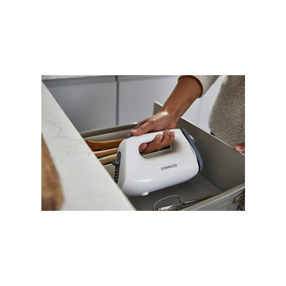 Eine Hand legt einen weißen Kenwood-Handmixer in eine Schublade mit Küchenutensilien.