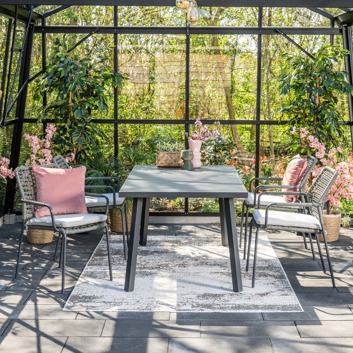 Een tafel en stoelen in een kas met planten en bloemen.