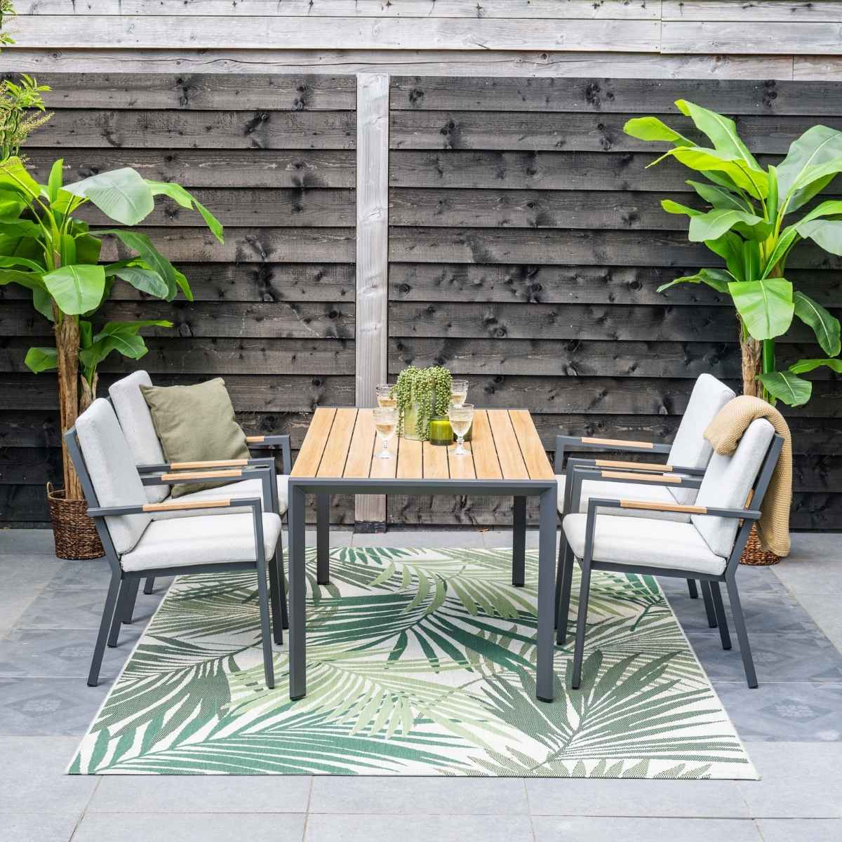Een tuinset met tafel, vier stoelen en een vloerkleed met palmbladeren.